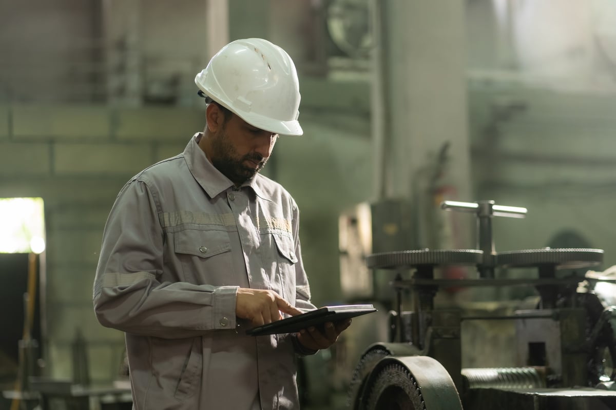 Engineer using a digital tablet to check data next to heavy machinery in a factory